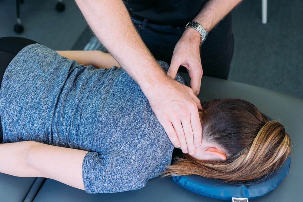 Physiotherapist at Integrity Physiotherapy Como providing hands-on neck treatment to client lying face down on treatment table.